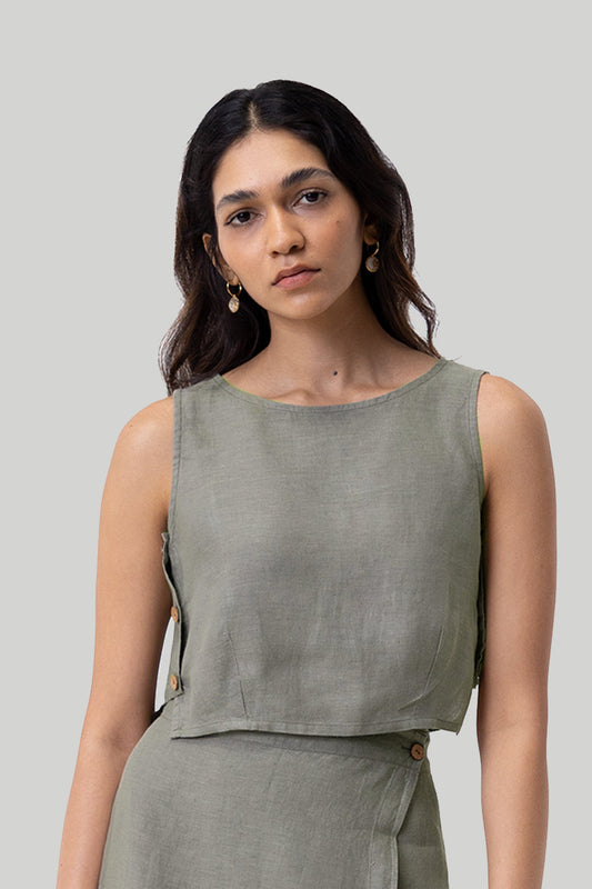 Woman wearing a green sleeveless top against a plain background Boxy crop top in dark green sustainable hemp with relaxed fit, side panel details and button accents