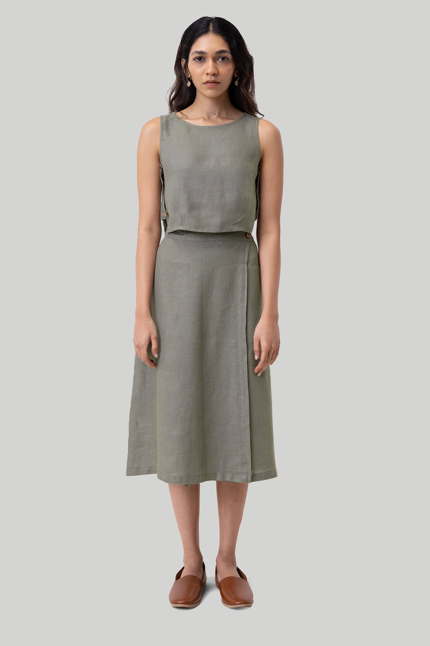 Woman wearing a sleeveless green top and skirt set on a plain background