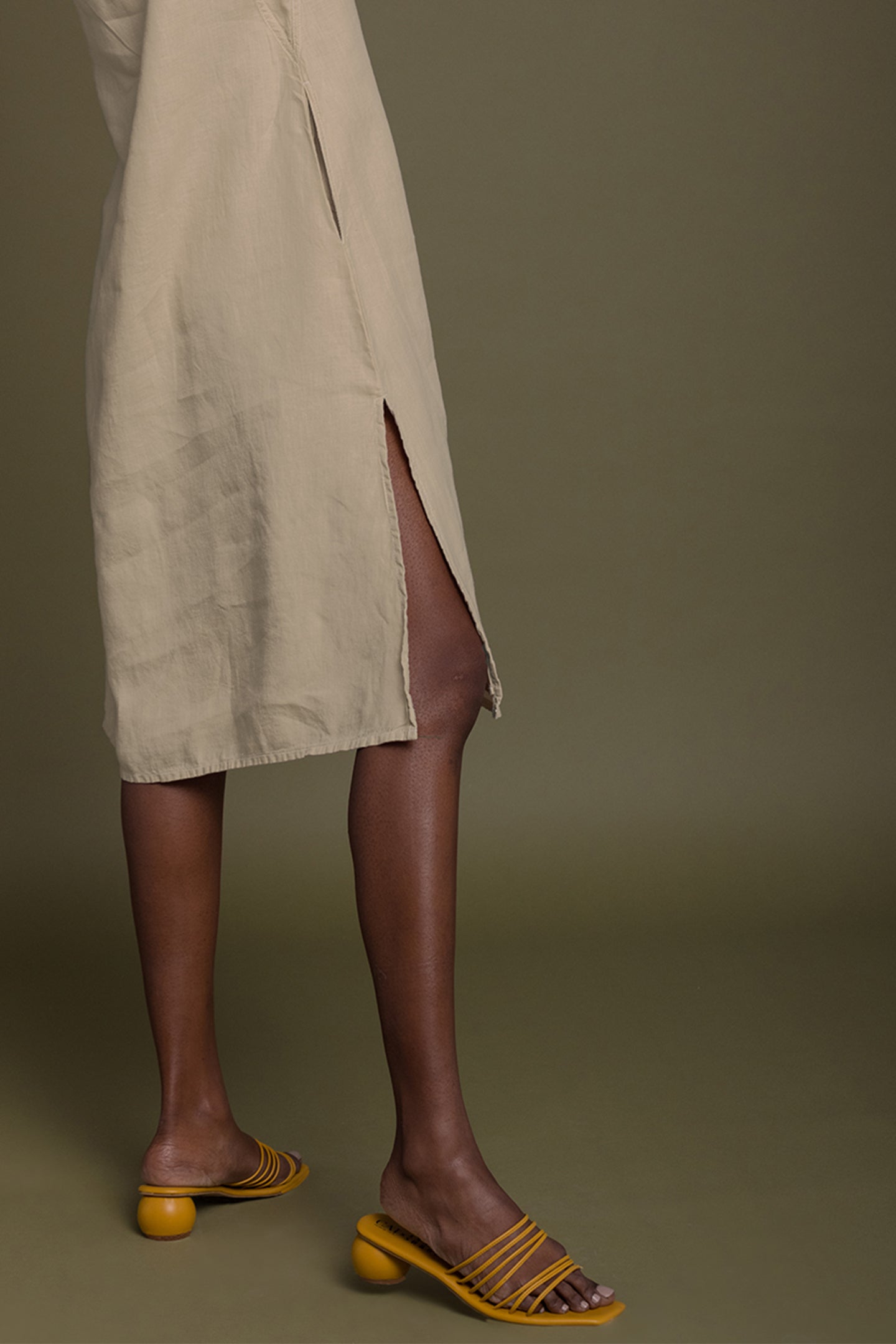Person wearing a beige dress and yellow sandals on a green background