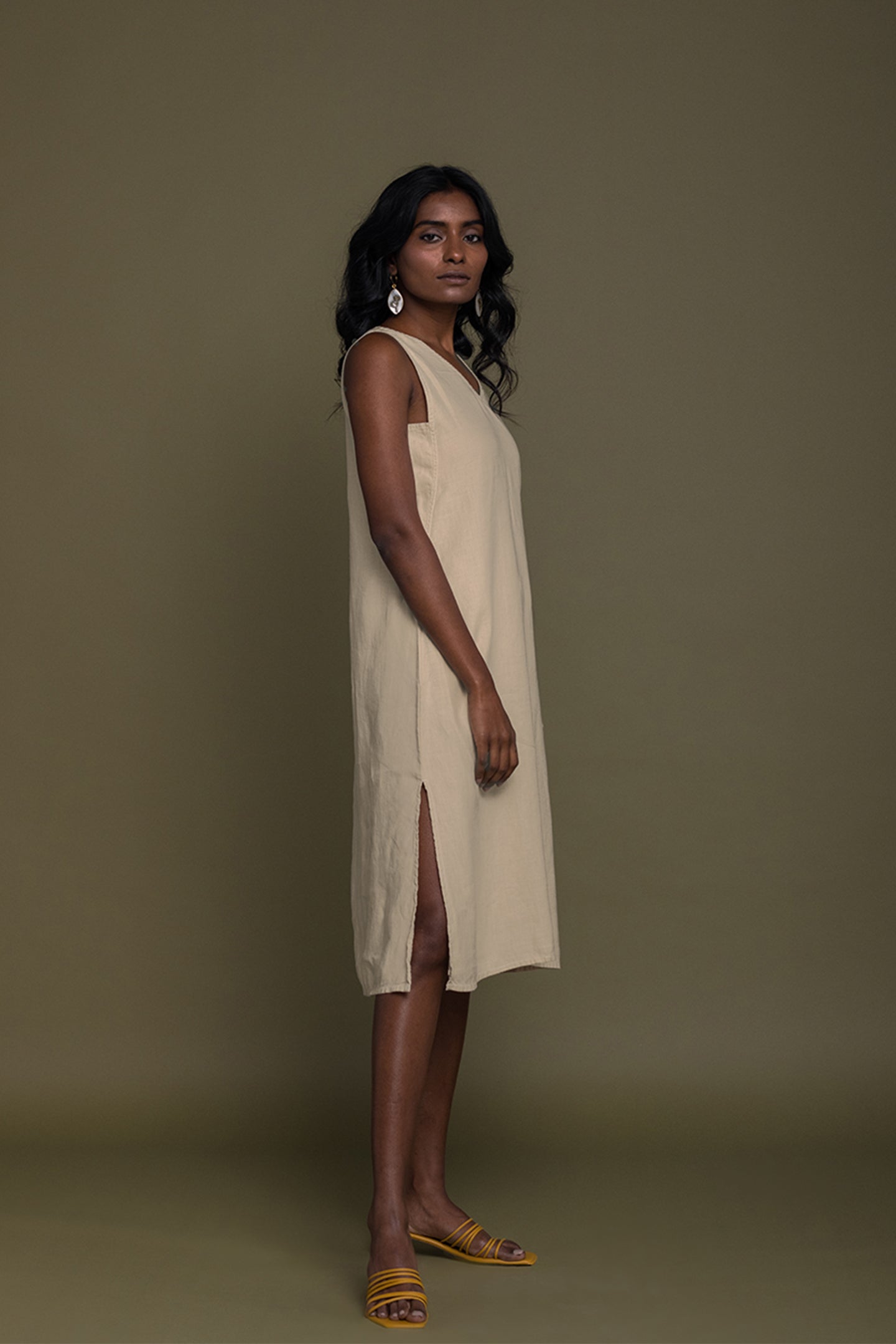 Woman wearing a beige sleeveless dress against a plain background Reading Tea Leaves midi dress in neutral beige sustainable hemp with A-line fit, side slits and practical pockets