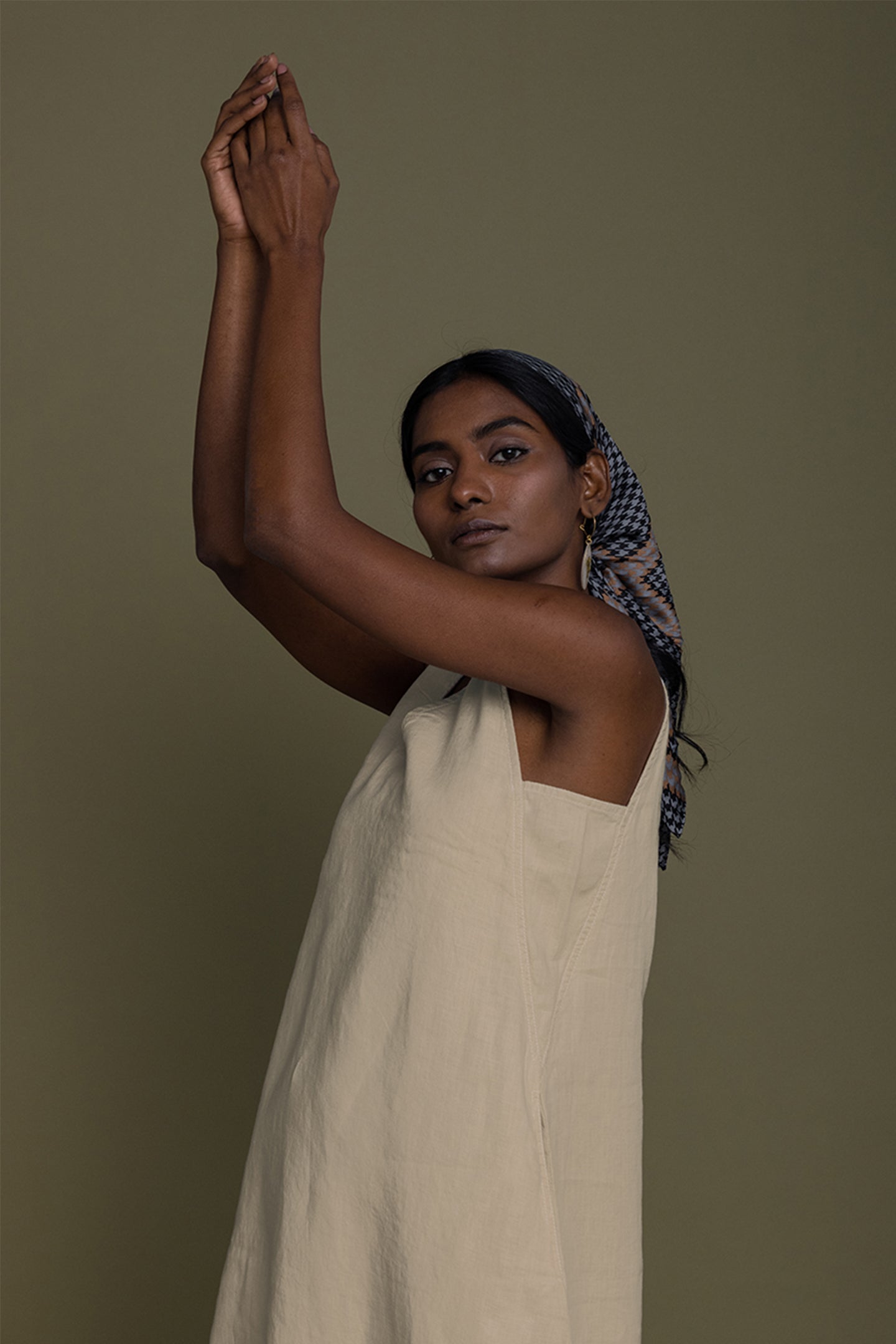 Woman in a beige dress with a headscarf against a brown background