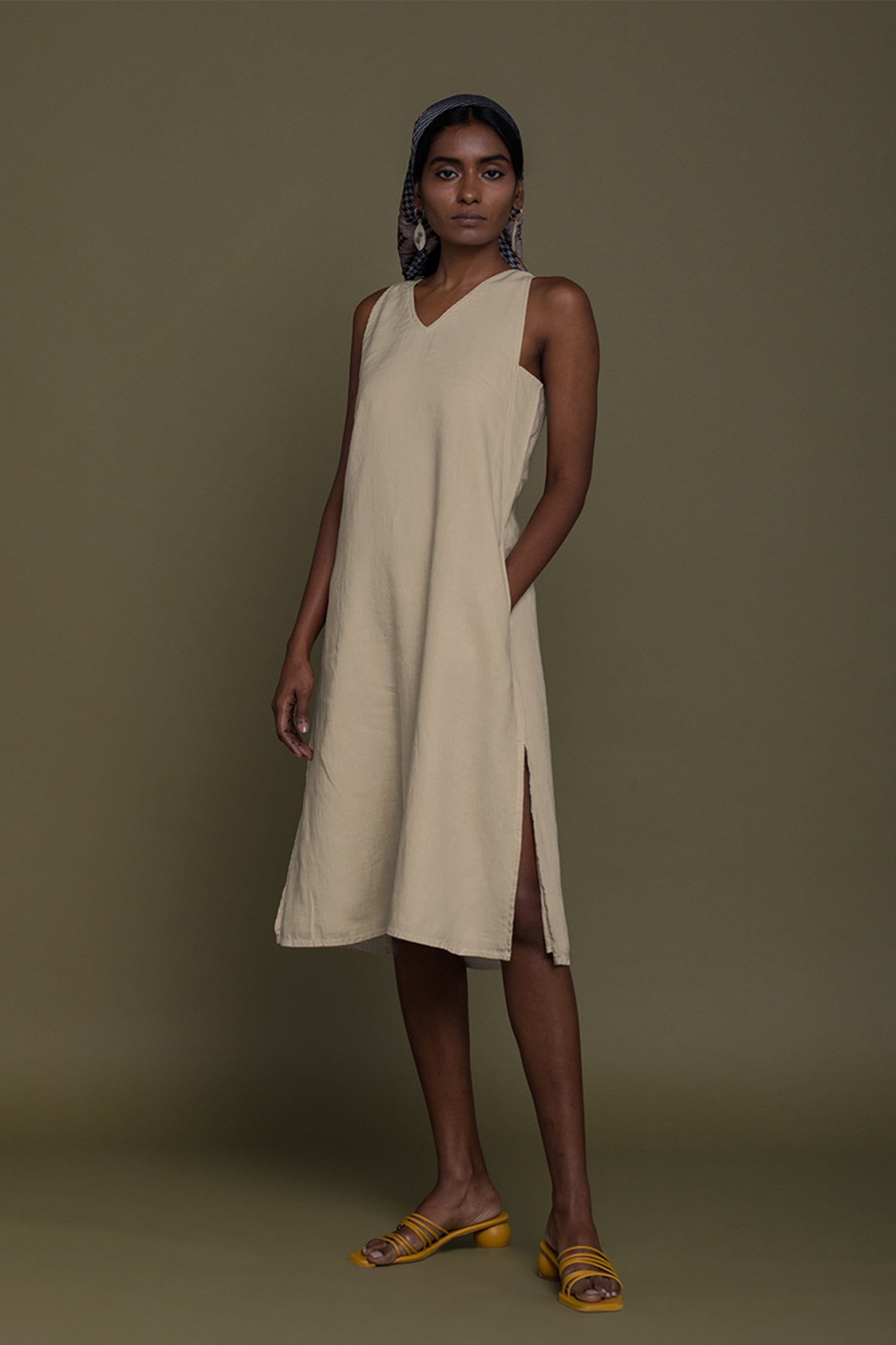 Woman wearing a beige sleeveless dress against a brown background