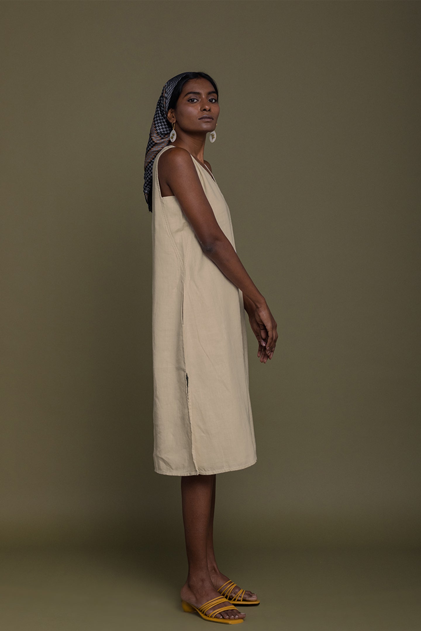 Woman wearing a beige dress against a green background Reading Tea Leaves midi dress in neutral beige sustainable hemp with A-line fit, side slits and practical pockets