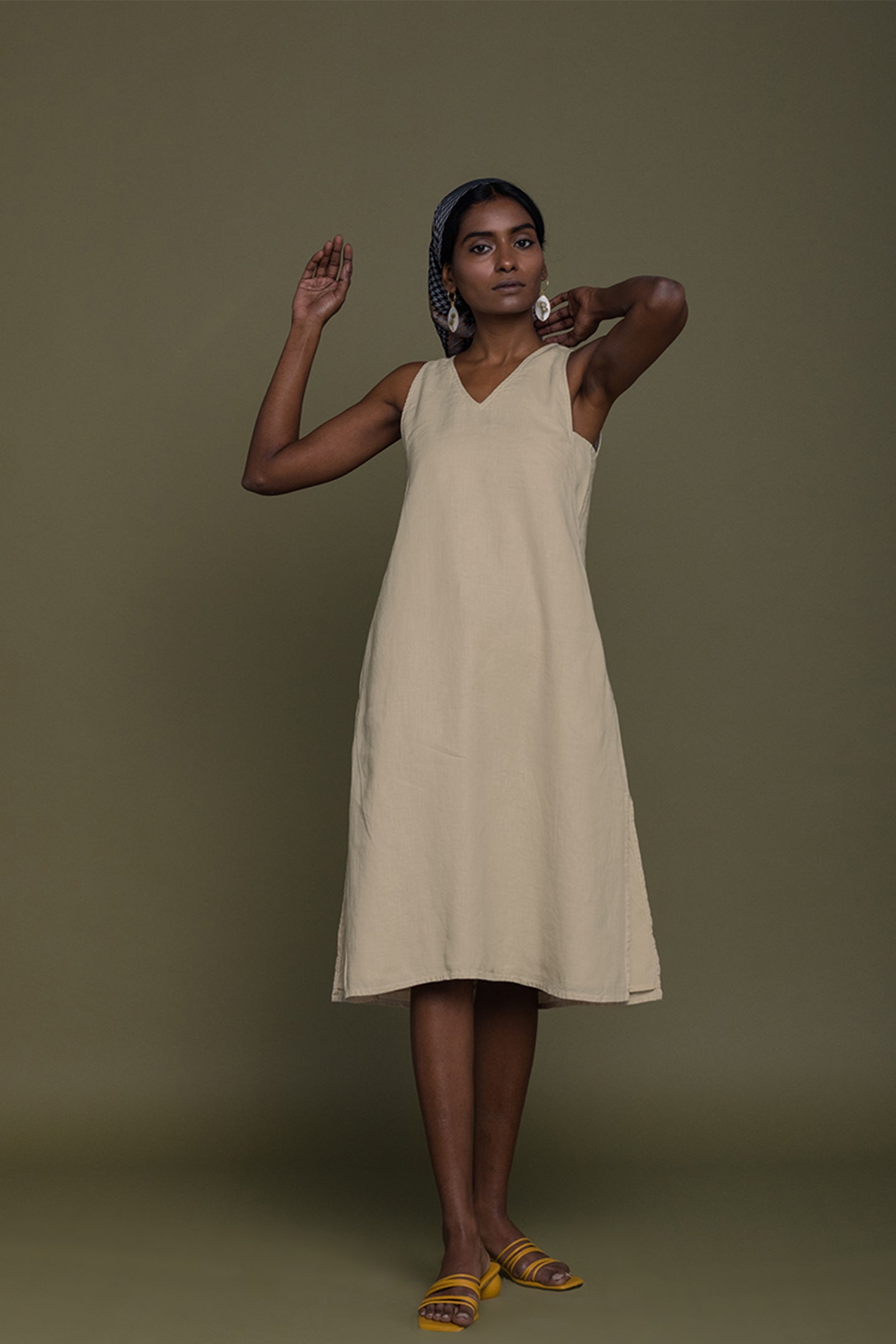 Woman wearing a beige sleeveless dress against a brown background
