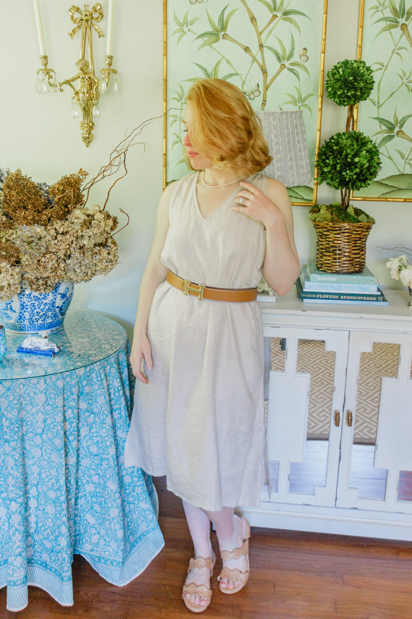 Woman in a beige dress standing in a decorated room with a table and decorative items.
