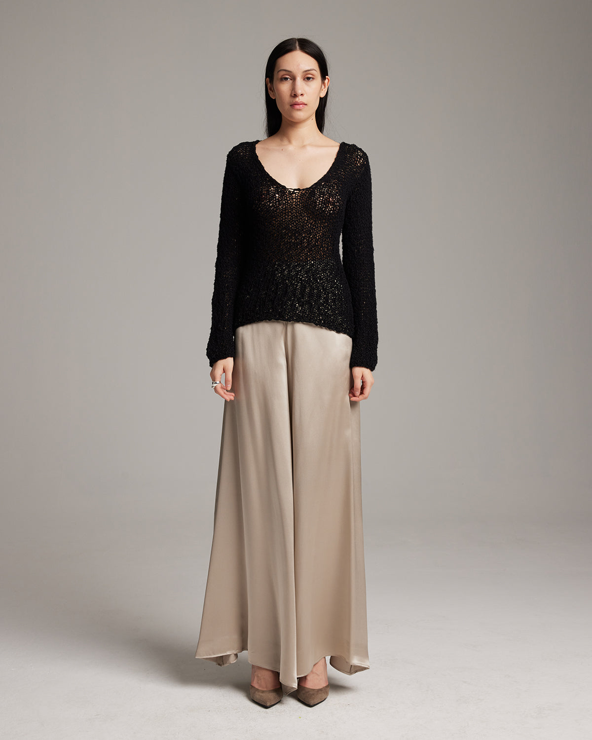 Woman wearing a black lace top and beige pants on a gray background Silk palazzo pants in flowing charmeuse with dramatic wide leg silhouette, ethically made in NYC by VOZ