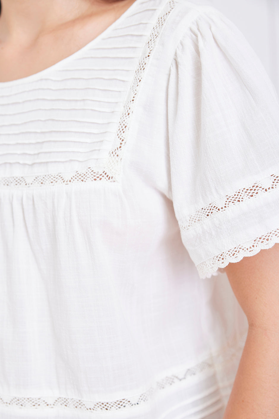 Close-up of a white top with lace trim on a plain background