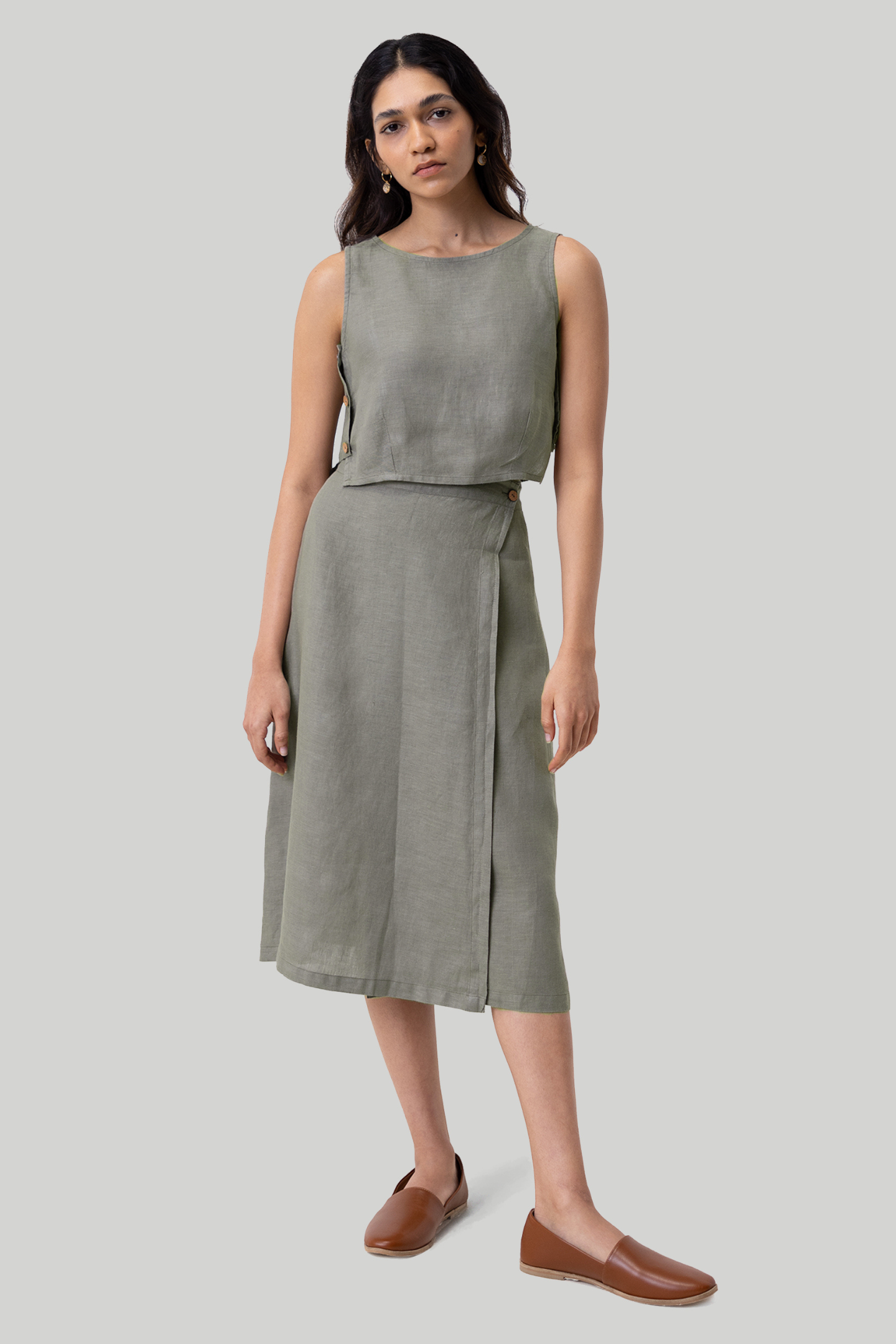 Woman wearing a sleeveless green top and skirt set on a gray background Boxy crop top in dark green sustainable hemp with relaxed fit, side panel details and button accents