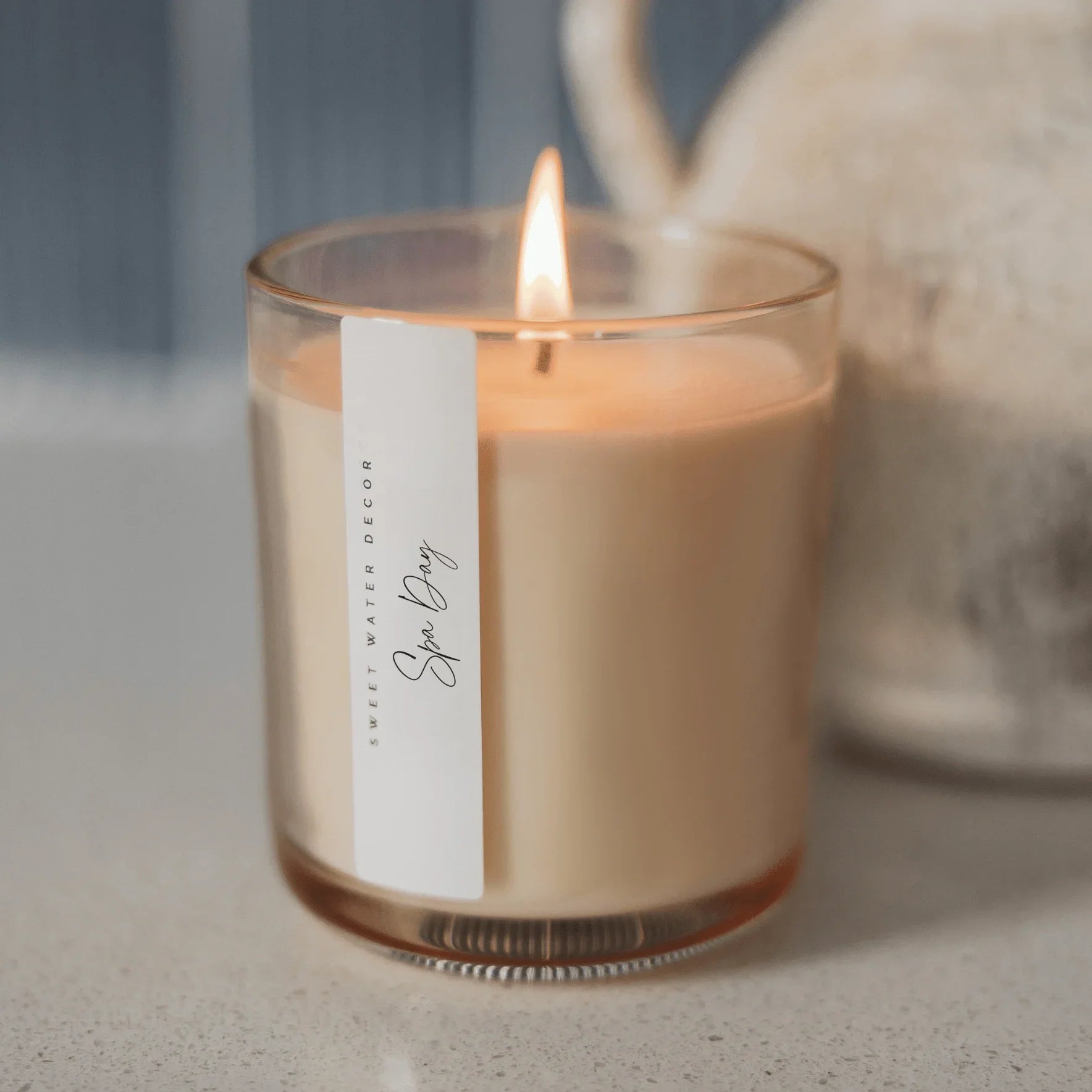 The 'Spa Day' scented soy candle by Sweet Water Decor, lit and glowing in its glass tumbler, from The Curated Home collection at Elizabeth and Bern.
