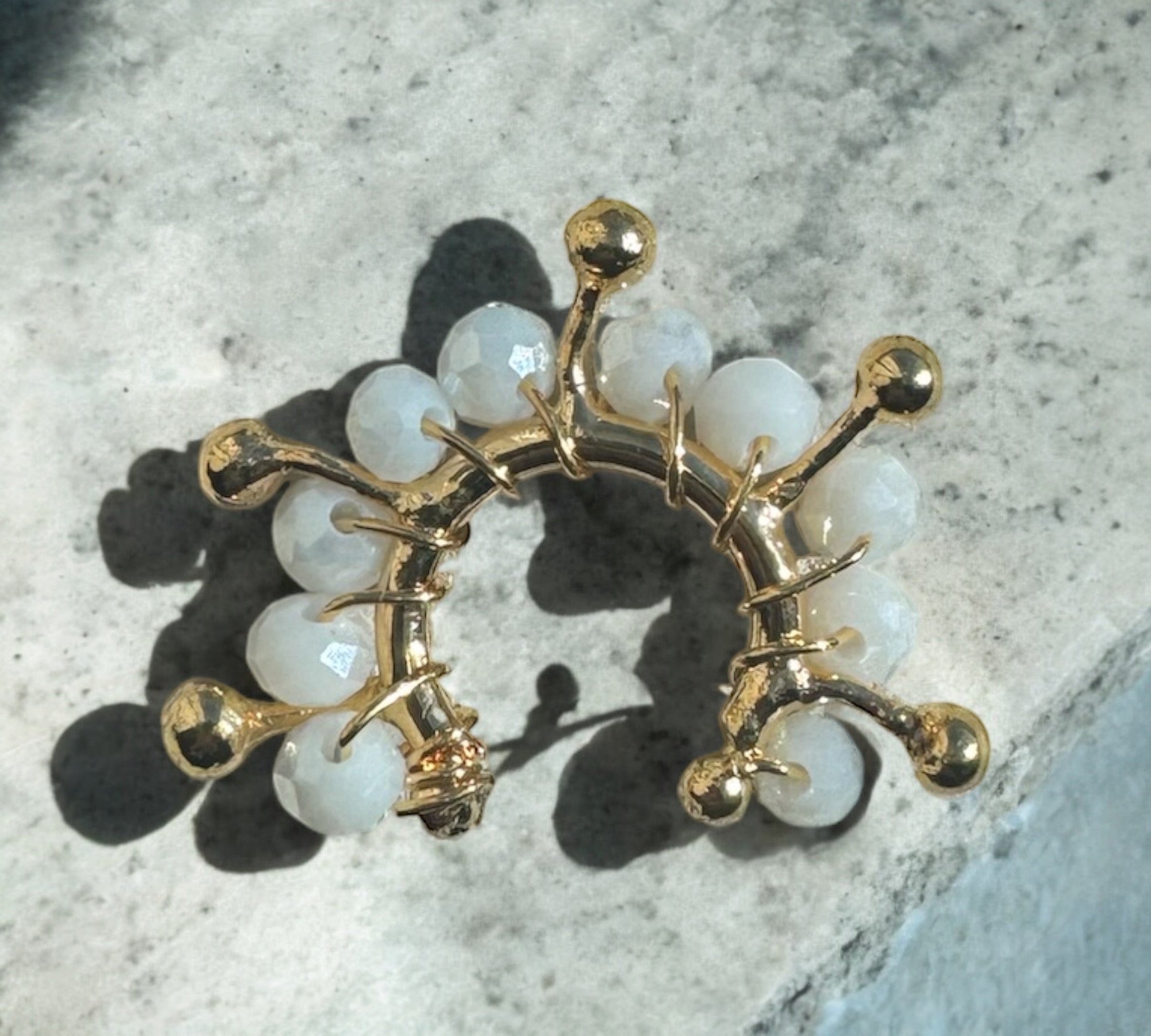 A sculptural gold ear cuff with white beads from the Heliconia Boutique artisan jewelry collection at Elizabeth and Bern.