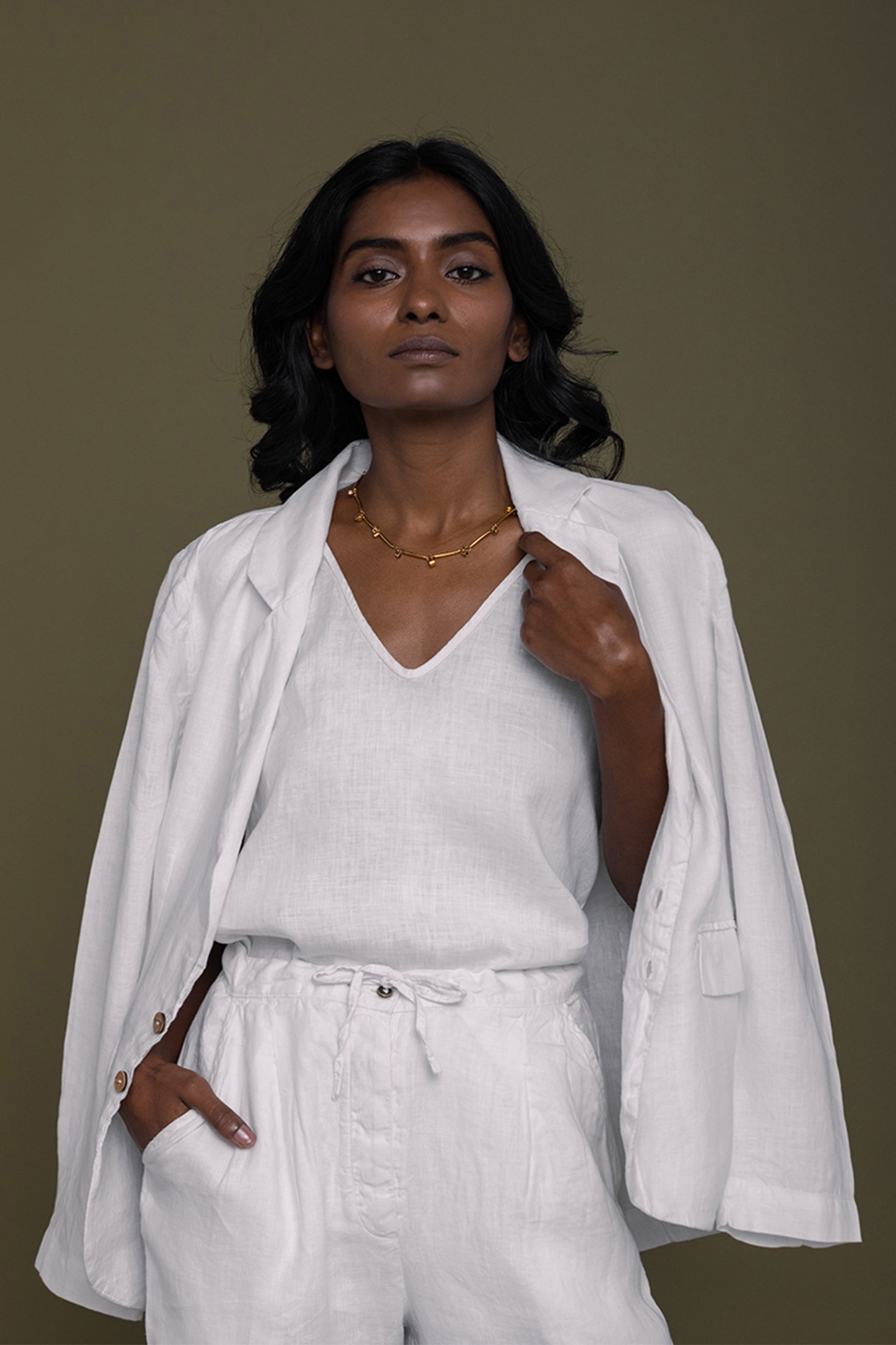 A woman wearing a sustainable white linen blazer and matching pants from the Reistor eco-friendly essentials collection at Elizabeth and Bern.”