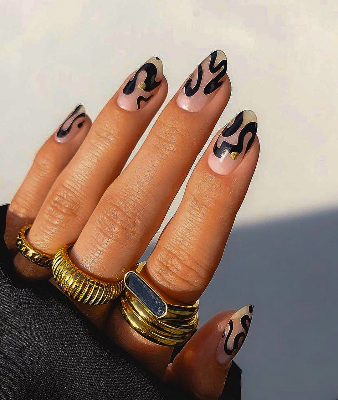 A hand with modern nail art wearing several gold-plated rings, including a thick ribbed ring, from the Guerilla Choice everyday luxury jewelry collection.