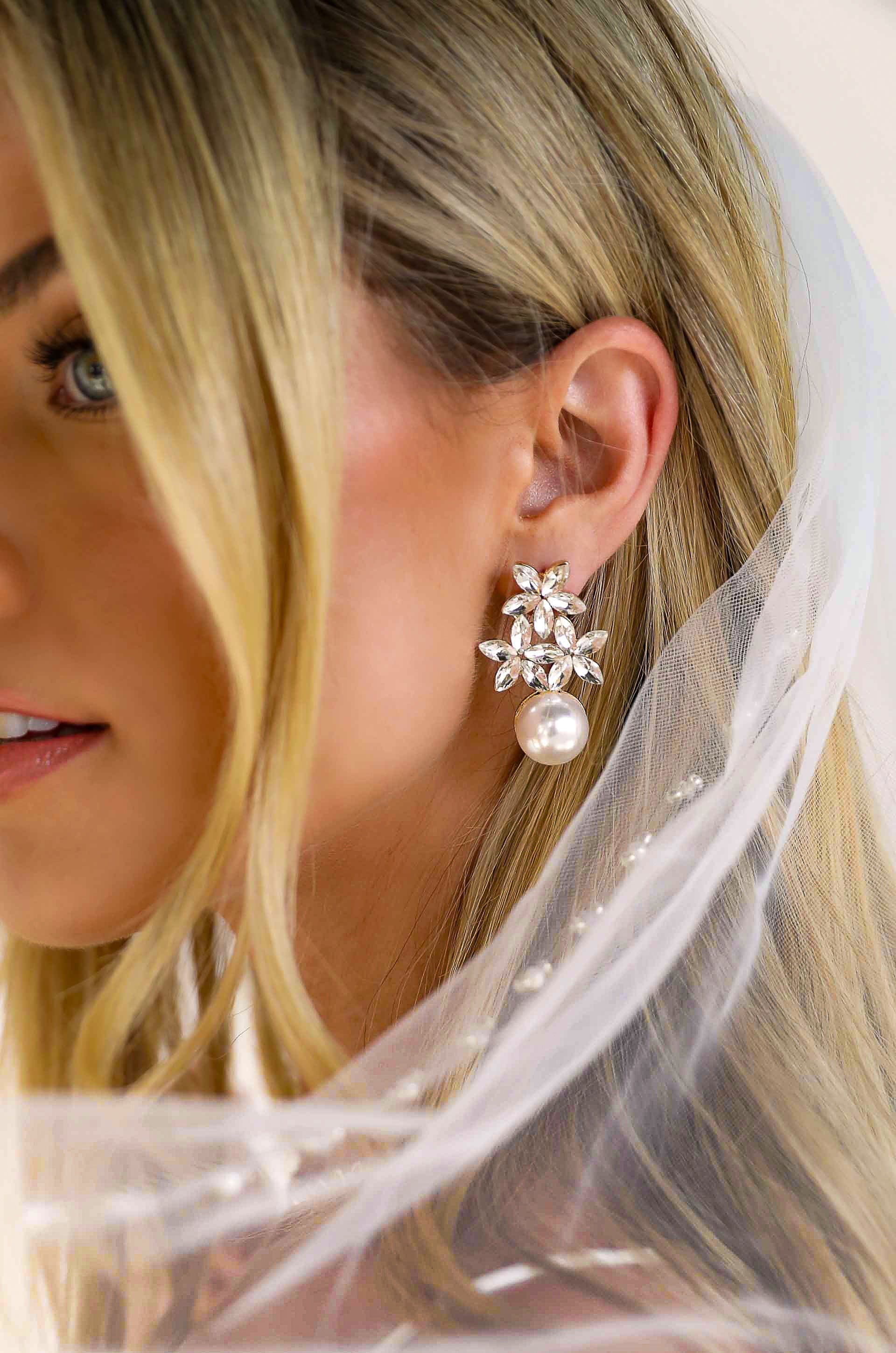 A bride wearing a pair of pearl and crystal statement floral earrings from the Ettika bridal and special occasion jewelry collection at Elizabeth and Bern.