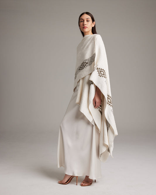 A woman wearing a beige, long, Estrella duster with geometric patterns, made of textured cotton, paired with a white dress.