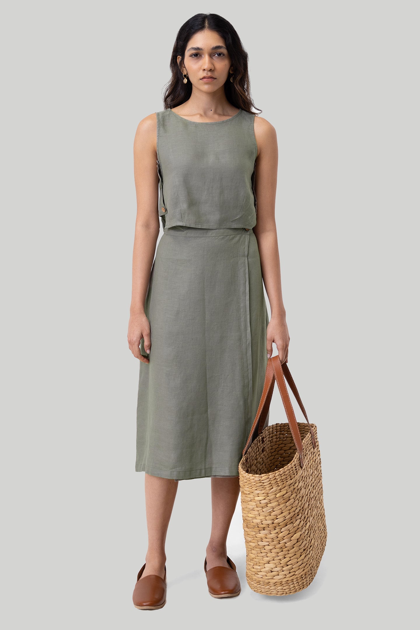 Woman wearing a green dress holding a woven bag on a plain background