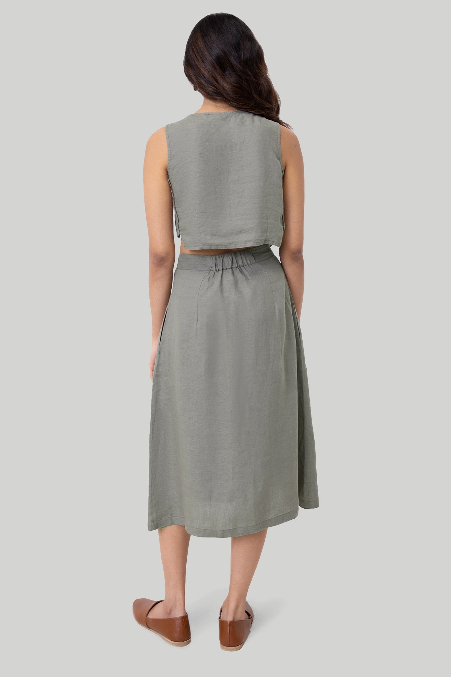 Woman wearing a green sleeveless top and skirt set on a light gray background Boxy crop top in dark green sustainable hemp with relaxed fit, side panel details and button accents


