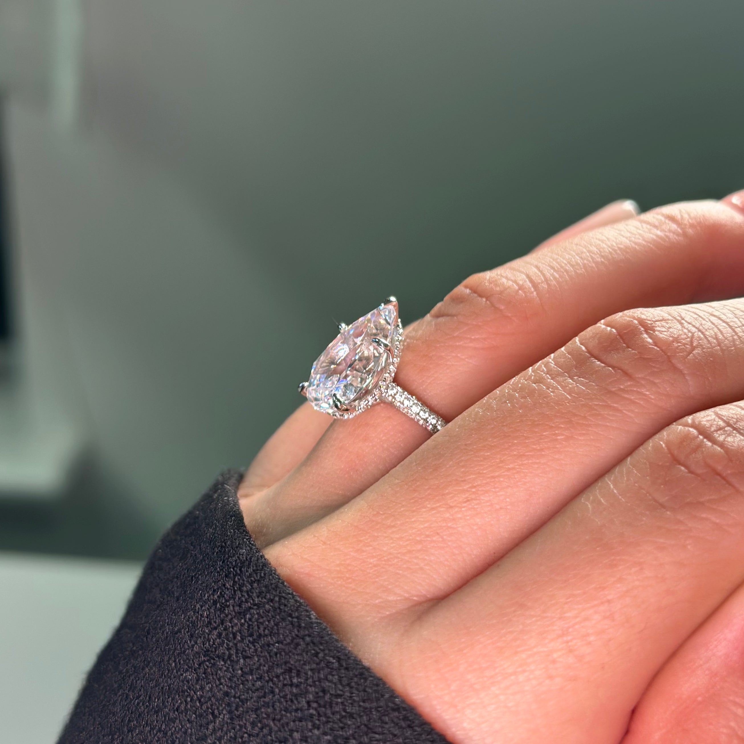Teardrop-shaped diamond ring on a hand with a blurred background
