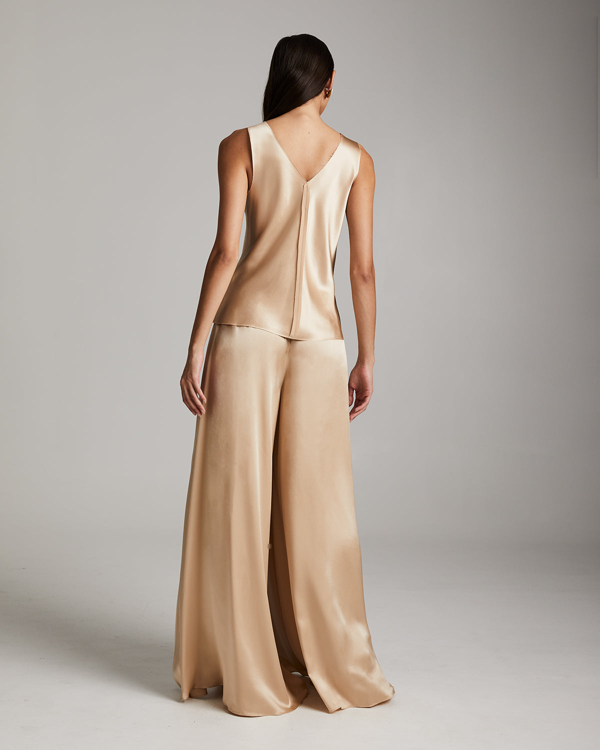 Woman wearing a beige satin outfit on a plain background Silk palazzo pants in flowing charmeuse with dramatic wide leg silhouette, ethically made in NYC by VOZ
