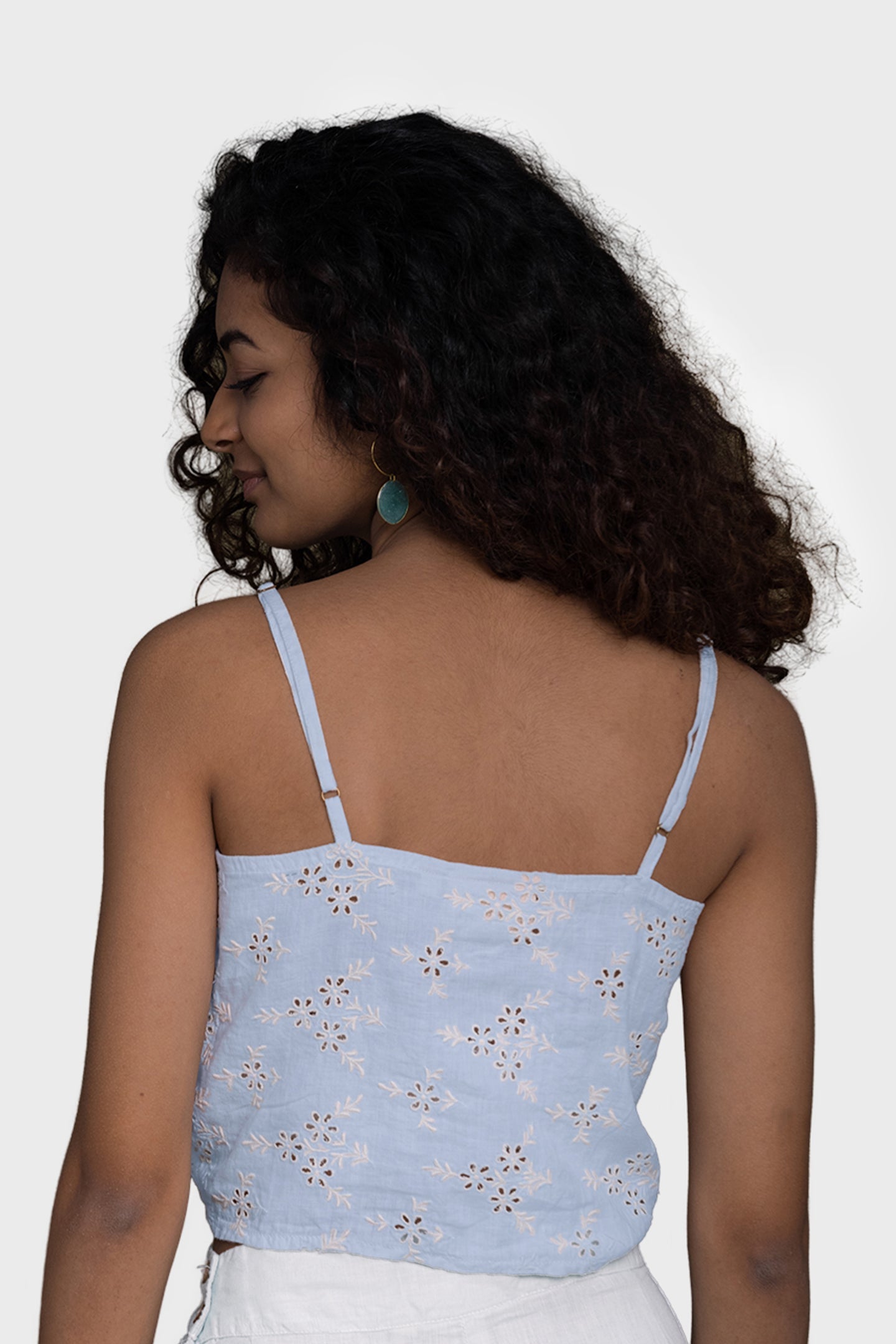 Woman wearing a light blue floral top against a white background Pool Day Tan Lines camisole top in summer blue hemp with eyelet embroidery, tie-up front and adjustable straps