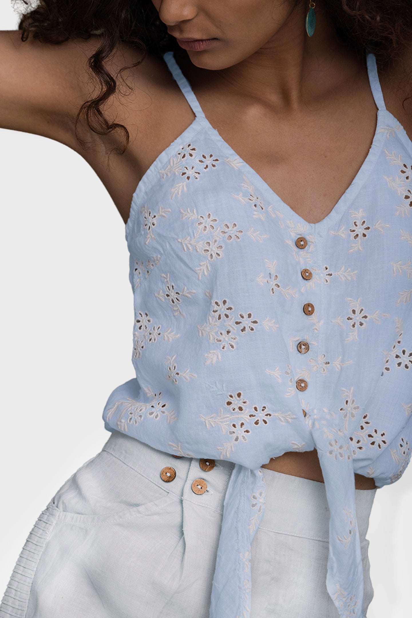 Light blue top with floral patterns and button details worn by a person on a plain background Pool Day Tan Lines camisole top in summer blue hemp with eyelet embroidery, tie-up front and adjustable straps