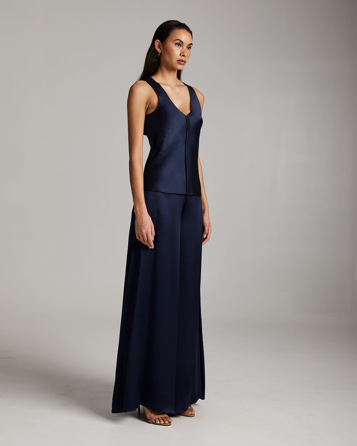 Woman wearing a navy blue sleeveless top and wide-leg pants on a gray background