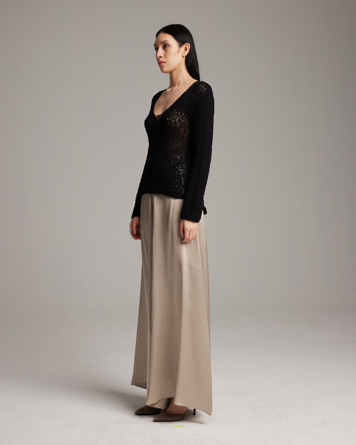 Woman wearing a black sequined top and beige pants on a plain background Silk palazzo pants in flowing charmeuse with dramatic wide leg silhouette, ethically made in NYC by VOZ