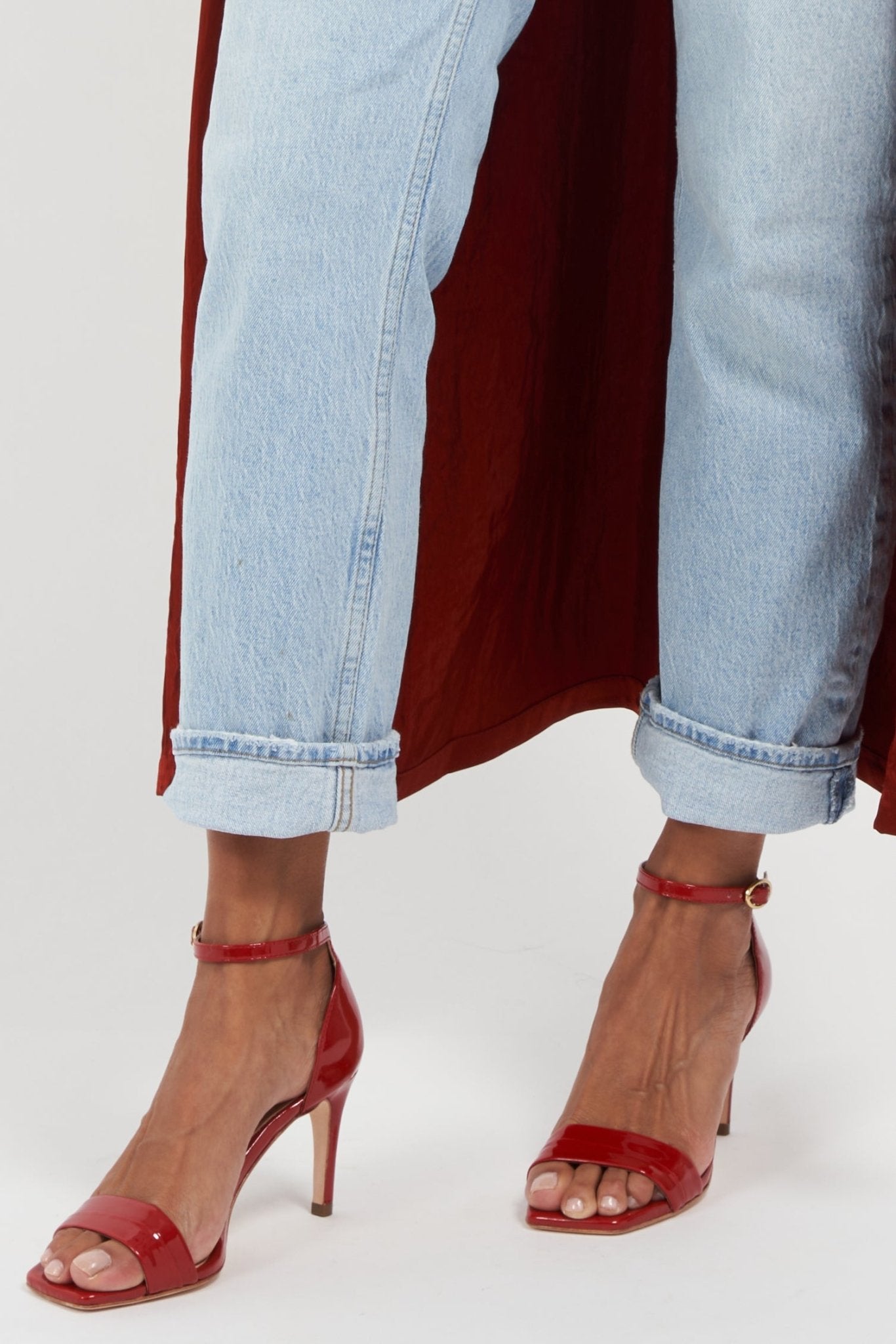 Red high-heeled sandals worn with light blue jeans on a white background