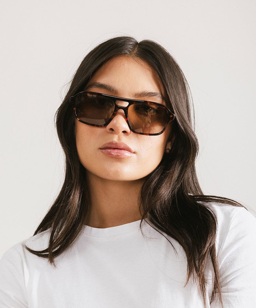 Woman wearing sunglasses and a white shirt against a plain background